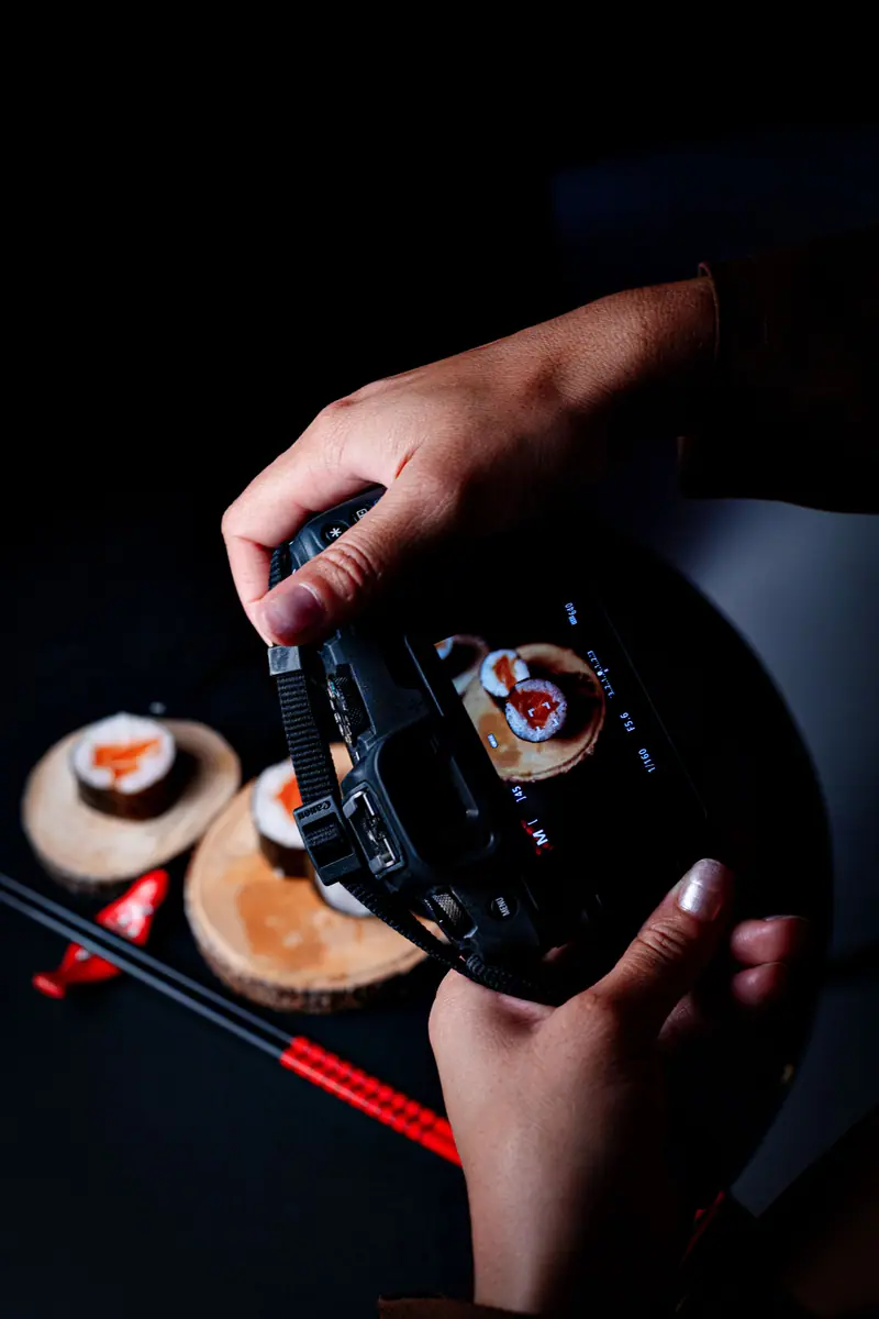Mãos segurando a câmera e fotografando sushi servido em tábuas de madeira