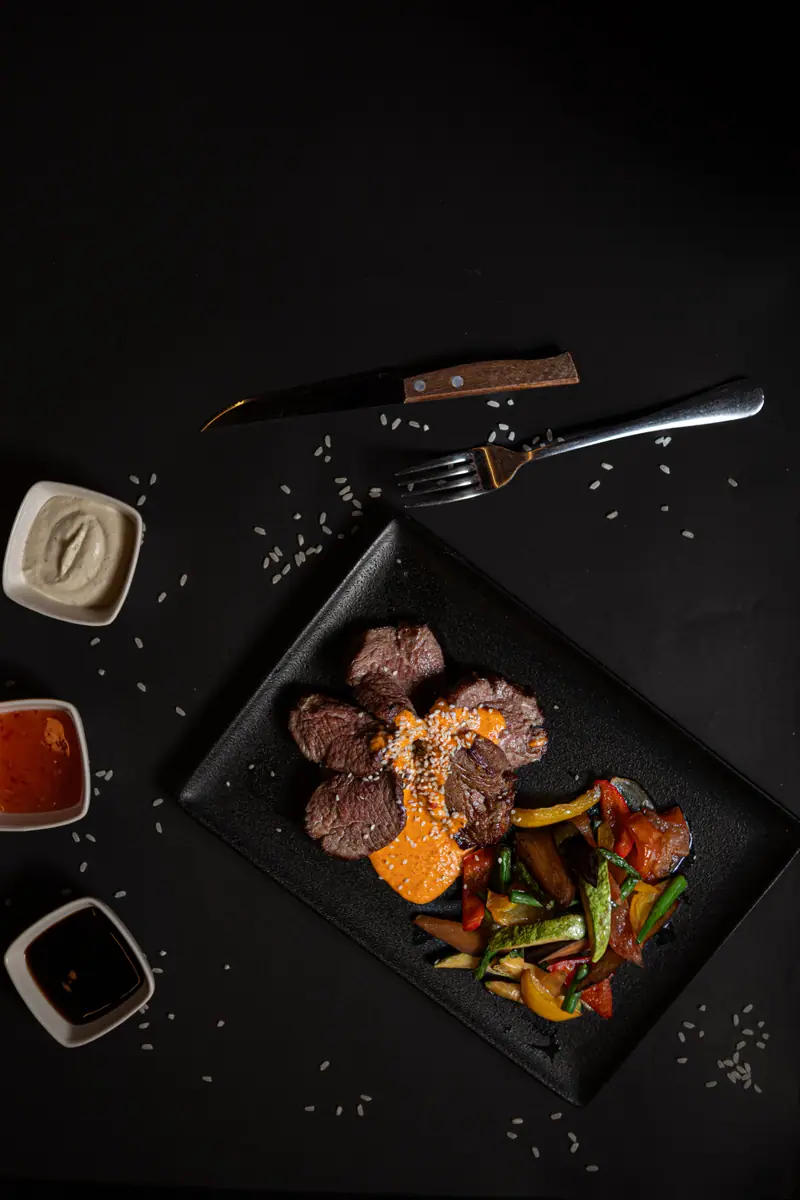 Carne fatiada sobre ardósia com molhos e talheres vistos de cima