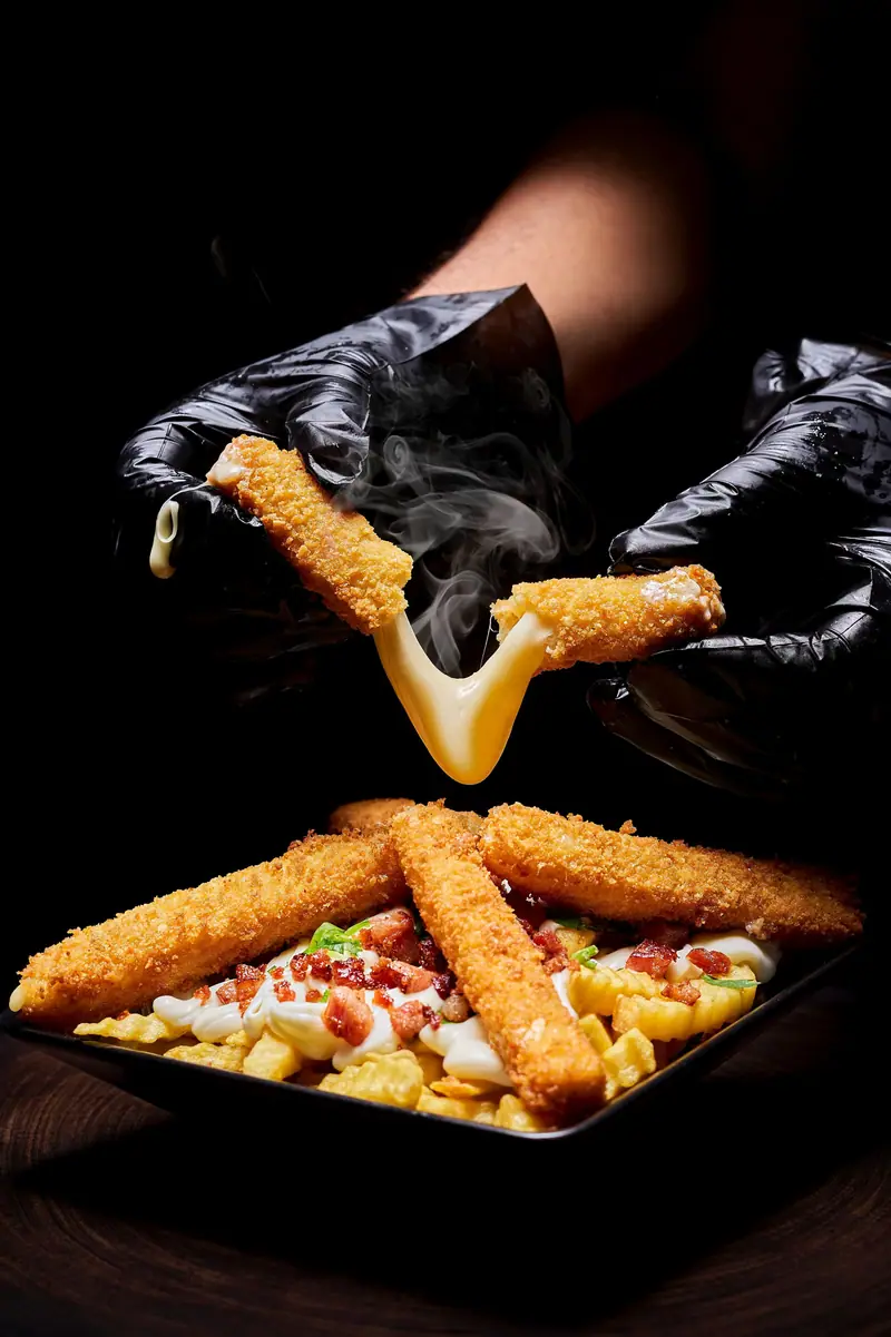 Mãos com luvas pretas partindo um empanado de queijo, com o queijo esticando